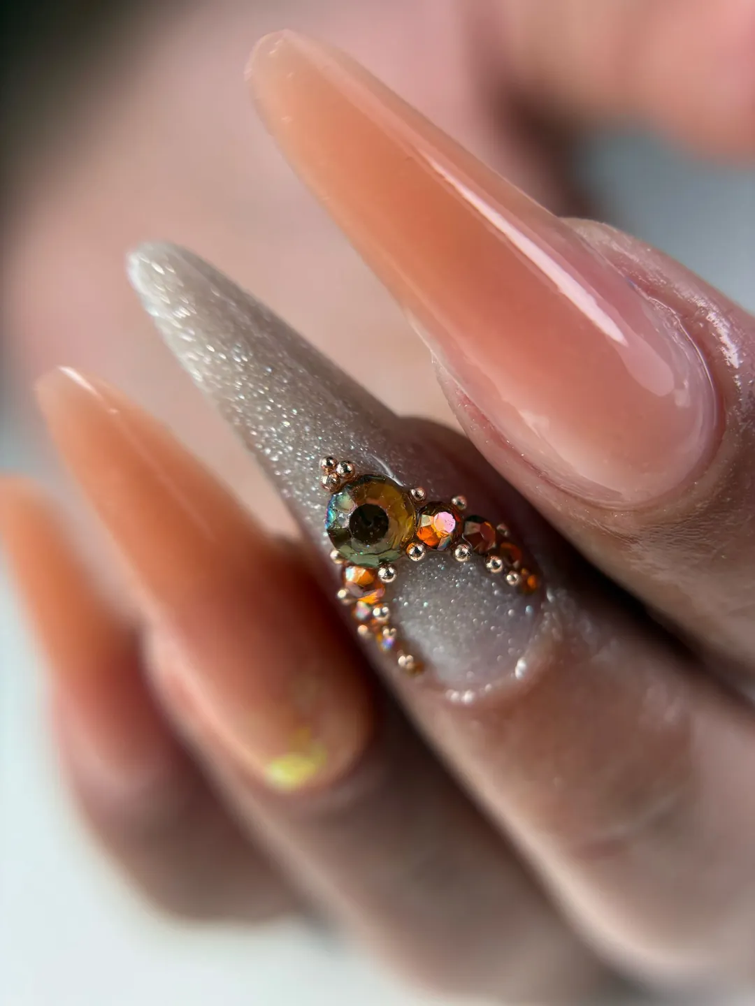 Uñas largas en forma almendra color nude con una uña de glitter y piedras